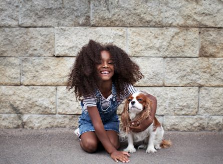 Smiling african american kid girl with dog outside. Happy child with pet
